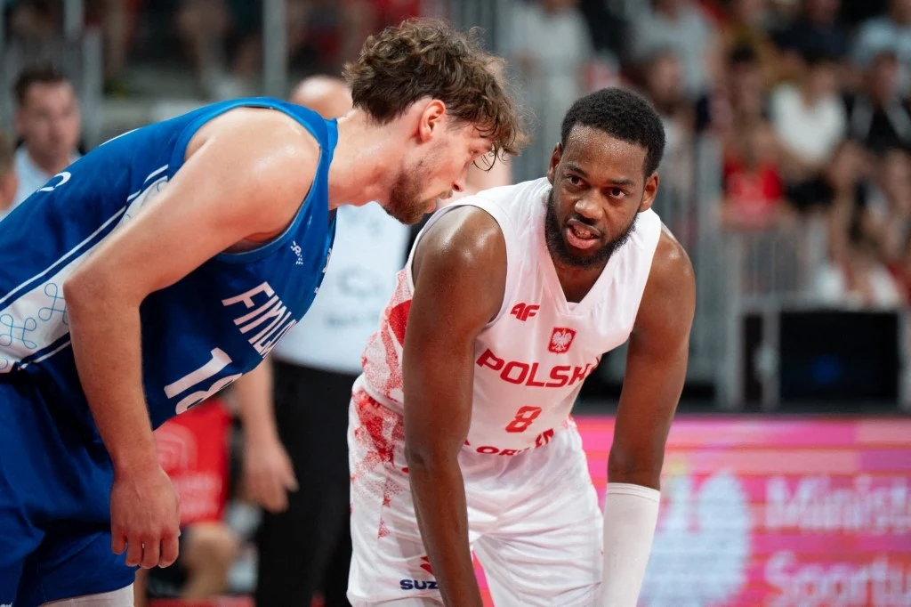 Jordan Loyd ma dać wiele radości polskim kibicom na Eurobaskecie Dwóch koszykarzy w trakcie meczu, jeden ubrany w biały strój z napisem Polska, drugi w niebieskim stroju z numerem 10, obaj koncentrują się na grze, a w tle widoczni kibice na trybunach.