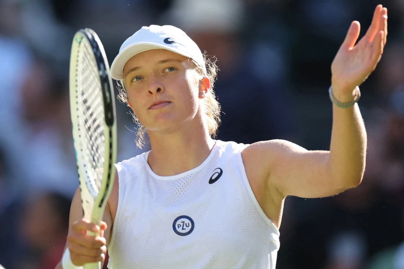 Iga Świątek Tenisistka w białym stroju i czapce sportowej z rakietą tenisową w dłoni, wykonująca gest ręką podczas meczu na korcie.