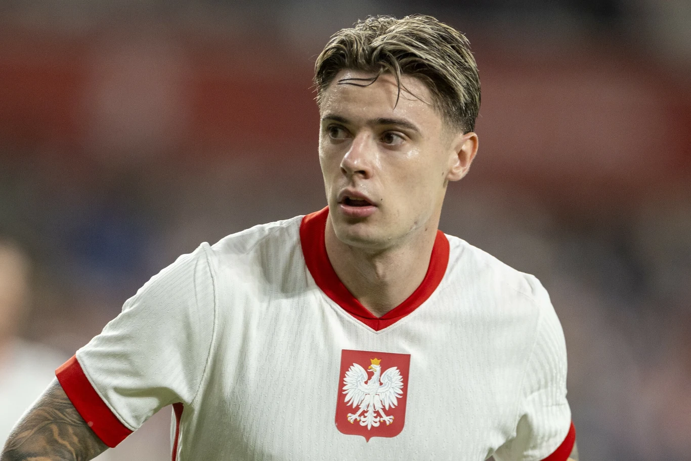 Nicola Zalewski Piłkarz w białej koszulce z czerwonym kołnierzem i godłem Polski na piersi w trakcie meczu, skupiony patrzy w bok, rozgrywając akcję sportową.