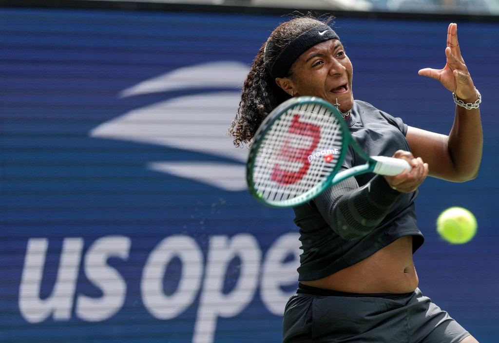 Hailey Baptiste Zawodniczka w trakcie dynamicznego uderzenia piłki tenisowej, intensywna ekspresja twarzy, tło z napisem US Open, skupienie na sporcie i rywalizacji.