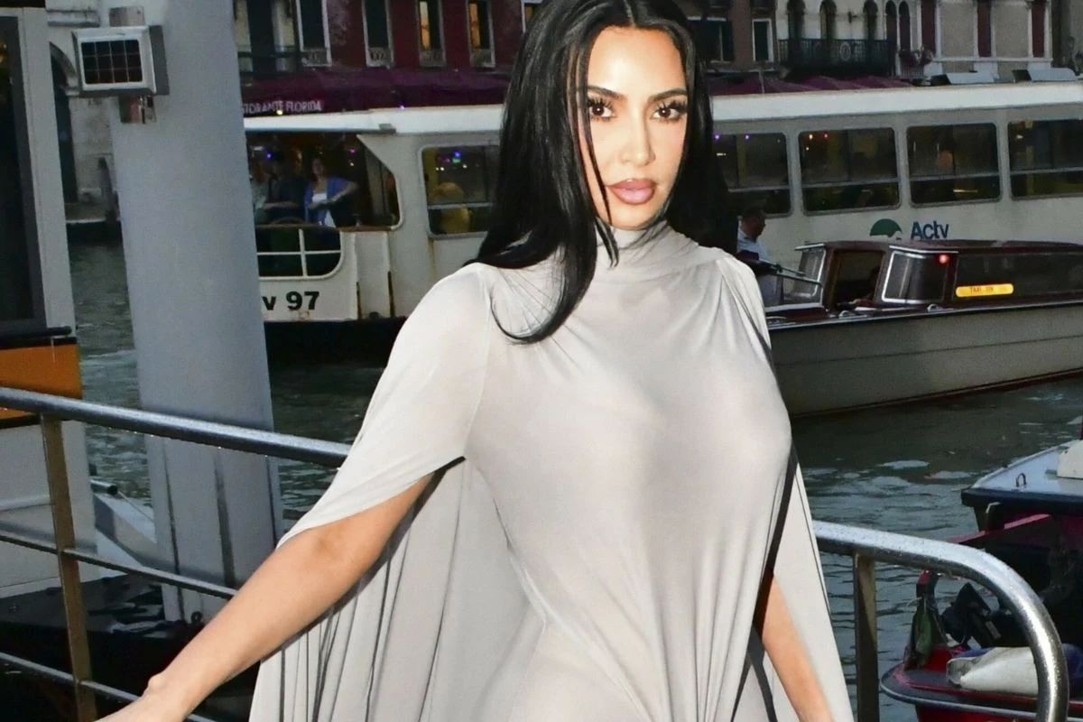 Kim Kardashian Kobieta z długimi czarnymi włosami ubrana w jasną, dopasowaną suknię z peleryną spaceruje w mieście w pobliżu kanału wodnego i łódki wycieczkowej.