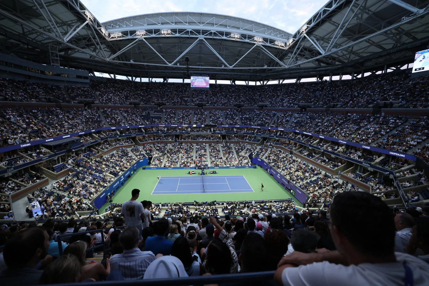 Arthur Ashe Stadium, główna arena zmagań w US Open. To tu w finale debla zabraknie pary numer 1 Kort tenisowy otoczony trybunami, pełnymi kibiców podczas dużego turnieju, zadaszona arena sportowa wypełniona widownią skupioną na meczu.