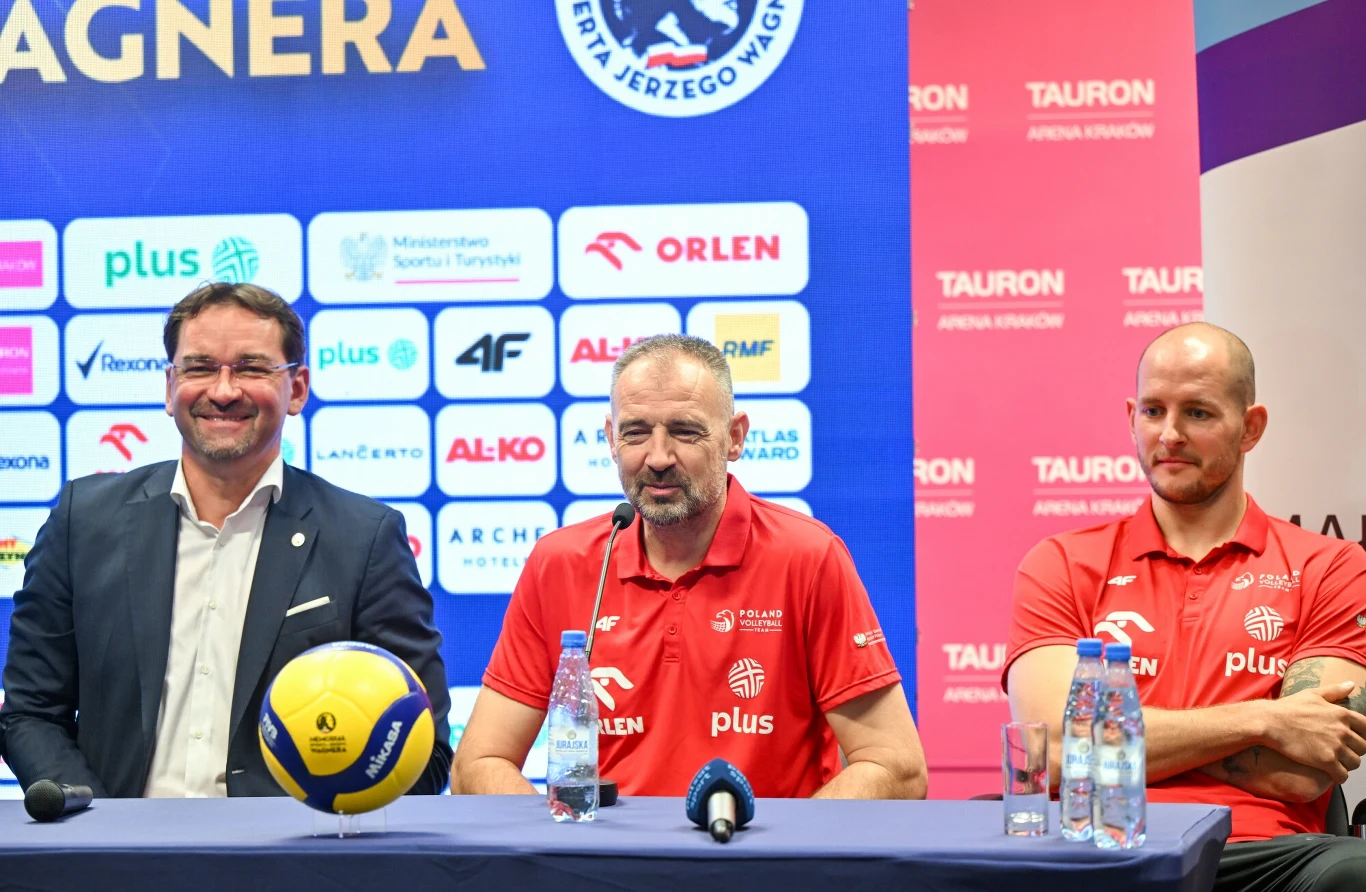 Od lewej: Sebastian Świderski, Nikola Grbić, Bartosz Kurek Trzech mężczyzn siedzi przy stole konferencyjnym, dwóch z nich ubranych jest w czerwone koszulki z logo sponsorów, przed nimi znajdują się mikrofony, piłka do siatkówki oraz butelki z wodą, w tle widoczna jest ściana z logo sponsorów wydarzenia sportow...