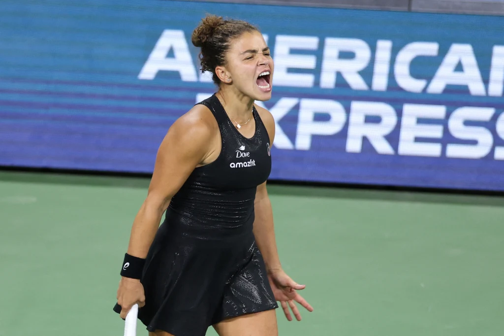 Jasmine Paolini Zawodniczka tenisowa w czarnej sportowej sukience okazuje silne emocje po zakończonej akcji na korcie, trzymając rakietę tenisową w lewej ręce, w tle widoczna reklama American Express.