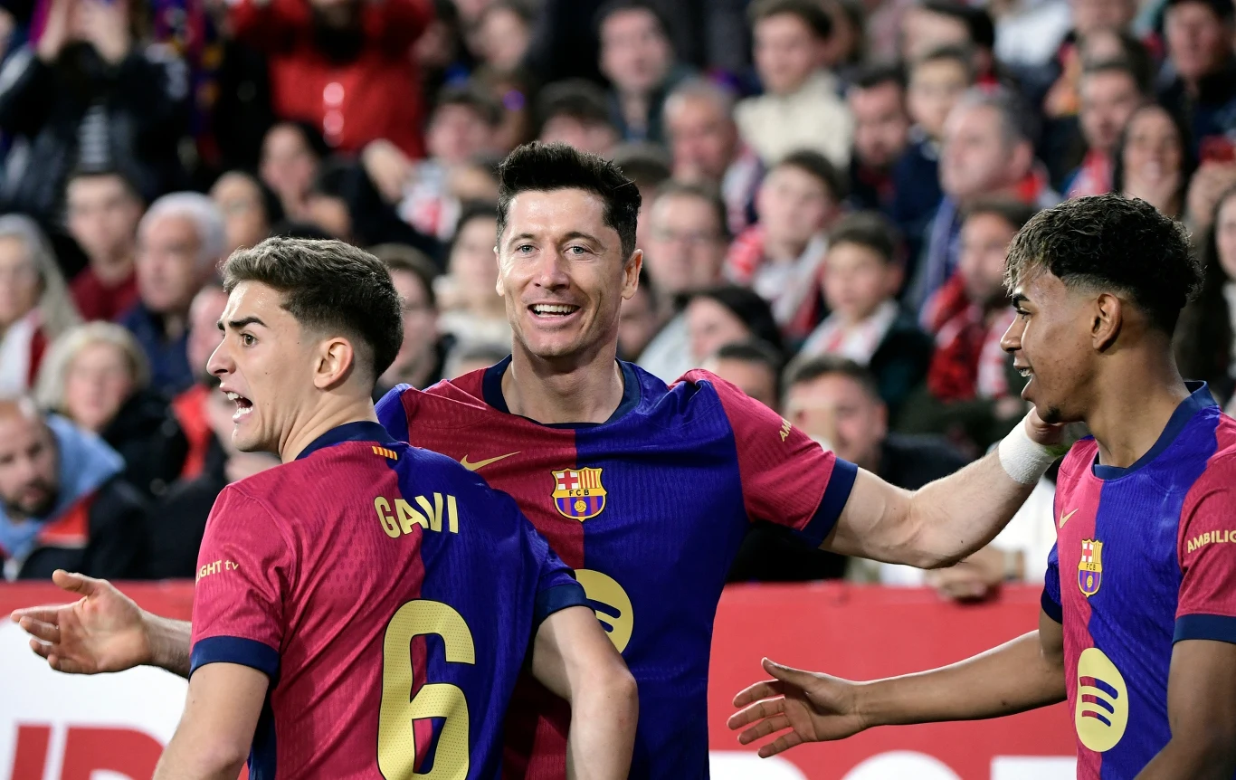 Trzech piłkarzy drużyny FC Barcelona w granatowo-bordo strojach cieszy się podczas meczu, w tle trybuny z kibicami.