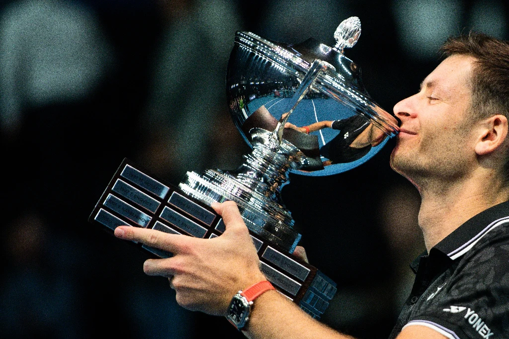 Hubert Hurkacz z pucharem za triumf w Marsylii w 2023 roku Sportowiec w czarnej koszulce obejmuje i całuje dużego, srebrnego pucharu z licznymi tabliczkami, wyrażając radość ze zwycięstwa.