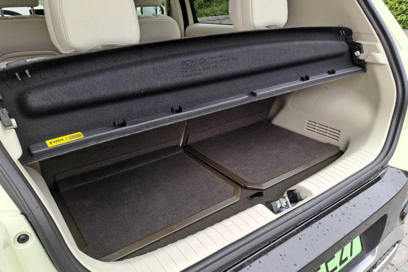 Bagażnik Hyundaia Instera ma 280 litrów. Po odsunięciu tylnych foteli maksymalnie do przodu przestrzeń ta rośnie do 351 litrów. Otwarty bagażnik samochodu z rozłożonym zabezpieczeniem przestrzeni bagażowej oraz dywanikami, widoczne jasne fotele tylne i fragment uszczelki klapy.