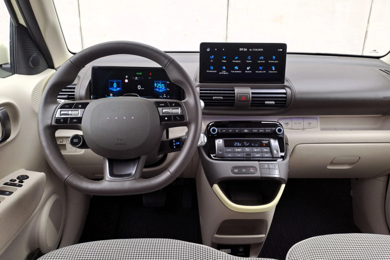 Wewnątrz Hyundaia Instera pozostawiono zaskakująco dużo fizycznych przełączników. Nowoczesne wnętrze samochodu elektrycznego z cyfrowym kokpitem, dużym wyświetlaczem na konsoli centralnej oraz ergonomicznie rozmieszczonymi przyciskami na kierownicy i panelu sterowania.