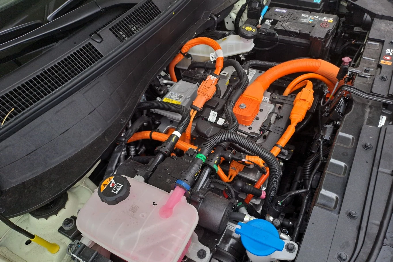 Hyundai Inster dostępny jest w dwóch wariantach mocy: 97 KM i 147 Nm oraz 115 KM i 147 Nm. Silnik oraz elementy instalacji elektrycznej samochodu elektrycznego z wyraźnie widocznymi pomarańczowymi przewodami wysokiego napięcia, akumulator, zbiornik płynu chłodniczego oraz inne komponenty pod maską pojazdu.