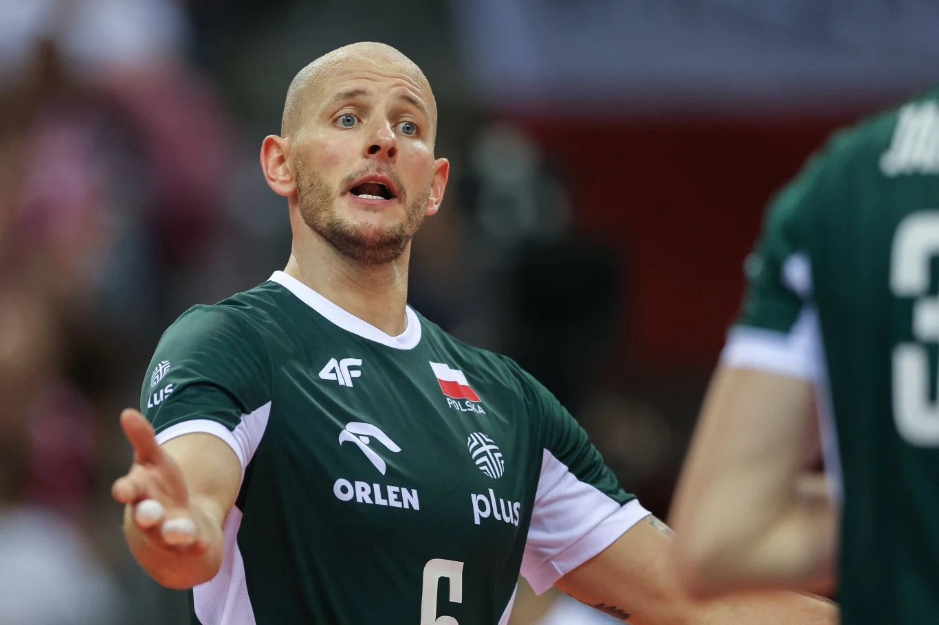 Siatkarz w zielonym stroju reprezentacji Polski z numerem 6, gestykulujący z wyrazem zdziwienia lub dyskusji, w tle rozmazani kibice lub inni zawodnicy.