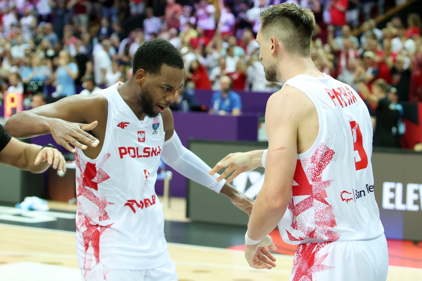 Jordan Loyd i Mateusz Ponitka w meczu przeciwko Izraelowi na EuroBaskecie 2025 Dwóch koszykarzy w białych strojach z czerwonymi akcentami świętuje na boisku podczas meczu, wokół nich widoczna rozentuzjazmowana publiczność.