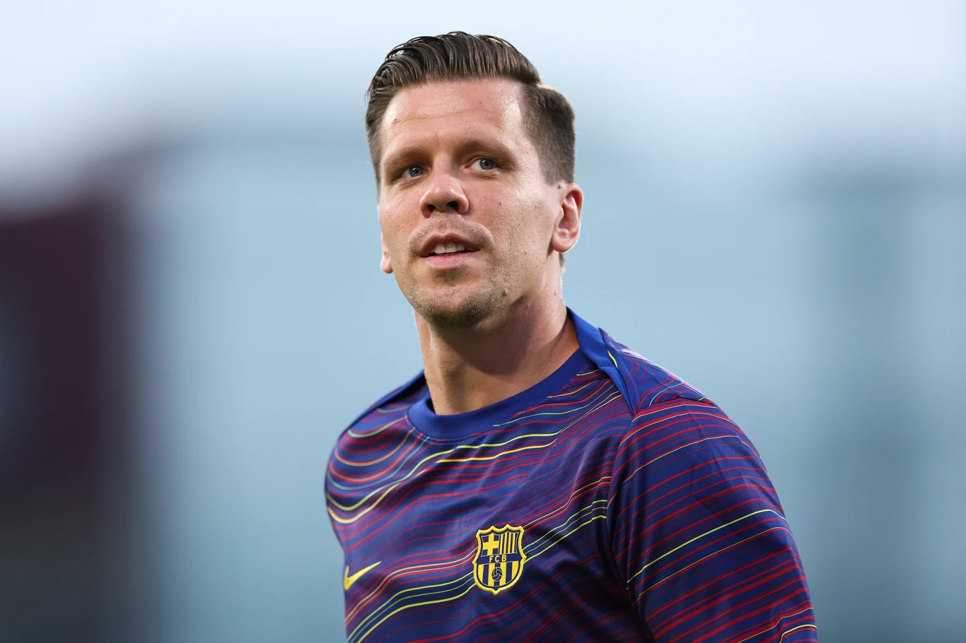 Wojciech Szczęsny Mężczyzna w sportowej koszulce w barwach FC Barcelona patrzy w dal, tło rozmyte, skupienie na twarzy i koszulce z herbem klubu.