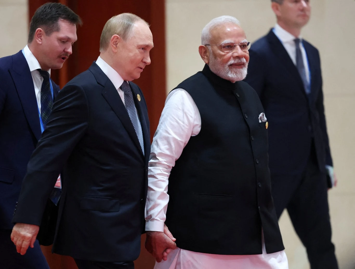 Władimir Putin i Narendra Modi podczas spotkania w Chinach Dwóch mężczyzn w oficjalnych strojach idzie obok siebie korytarzem, jeden z nich ubrany w garnitur, drugi w tradycyjny strój indyjski, wokół nich dwóch innych mężczyzn w garniturach.