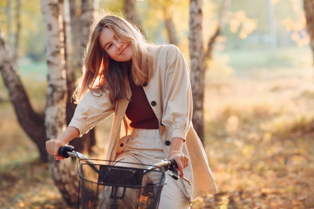 To jedna z twoich cyfr w numerze PESEL? Mają ją tylko urodzeni przywódcy Uśmiechnięta młoda kobieta oparta o rower, w jasnym ubraniu, na tle jesiennego, słonecznego lasu brzozowego.