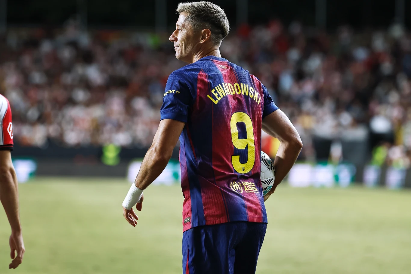 Piłkarz w koszulce FC Barcelony z numerem 9 trzyma piłkę przy linii bocznej boiska podczas meczu, w tle publiczność na stadionie.