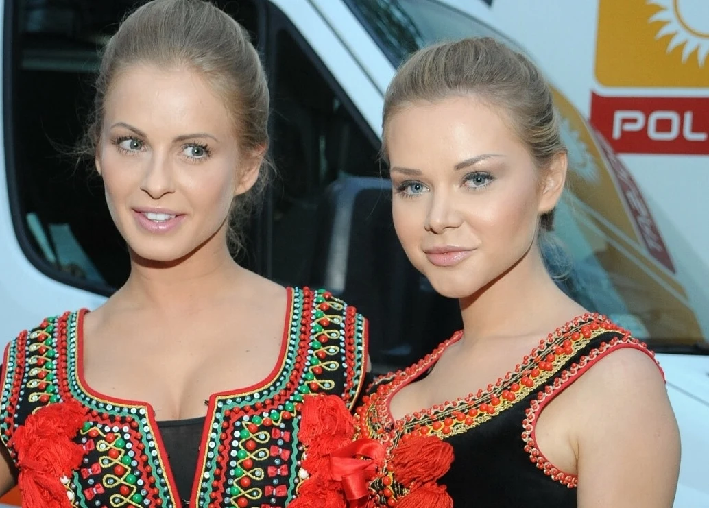 Paula Tumala i Ola Ciupa wystąpiły jako "Słowianki" u boku Cleo na Eurowizji Dwie młode kobiety ubrane w stroje ludowe z bogatymi zdobieniami i czerwonymi akcentami pozują razem do zdjęcia na tle białego pojazdu z logo.