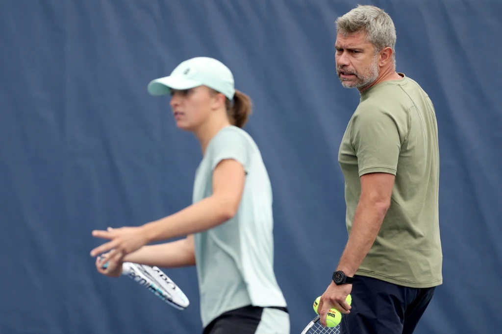 Iga Świątek i Tomasz Wiktorowski Dwie osoby na korcie tenisowym przygotowujące się do treningu, jedna trzyma rakietę tenisową, druga piłki tenisowe.