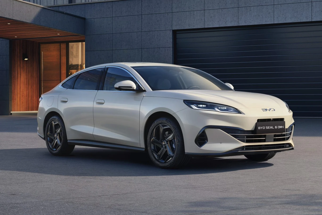 Nowoczesny elektryczny sedan BYD Seal 6 sprawiający wrażenie luksusu, zaparkowany przed nowoczesnym budynkiem z dużym garażem, podkreślające elegancki design oraz gładkie linie nadwozia samochodu.