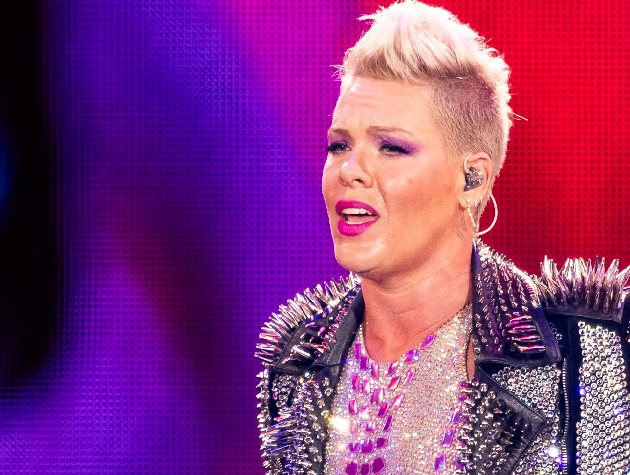 Pink kuruje się po zakażeniu Artystka podczas występu na scenie, ubrana w kurtkę ozdobioną ćwiekami, z wyrazistą fryzurą i makijażem, na tle kolorowych świateł.