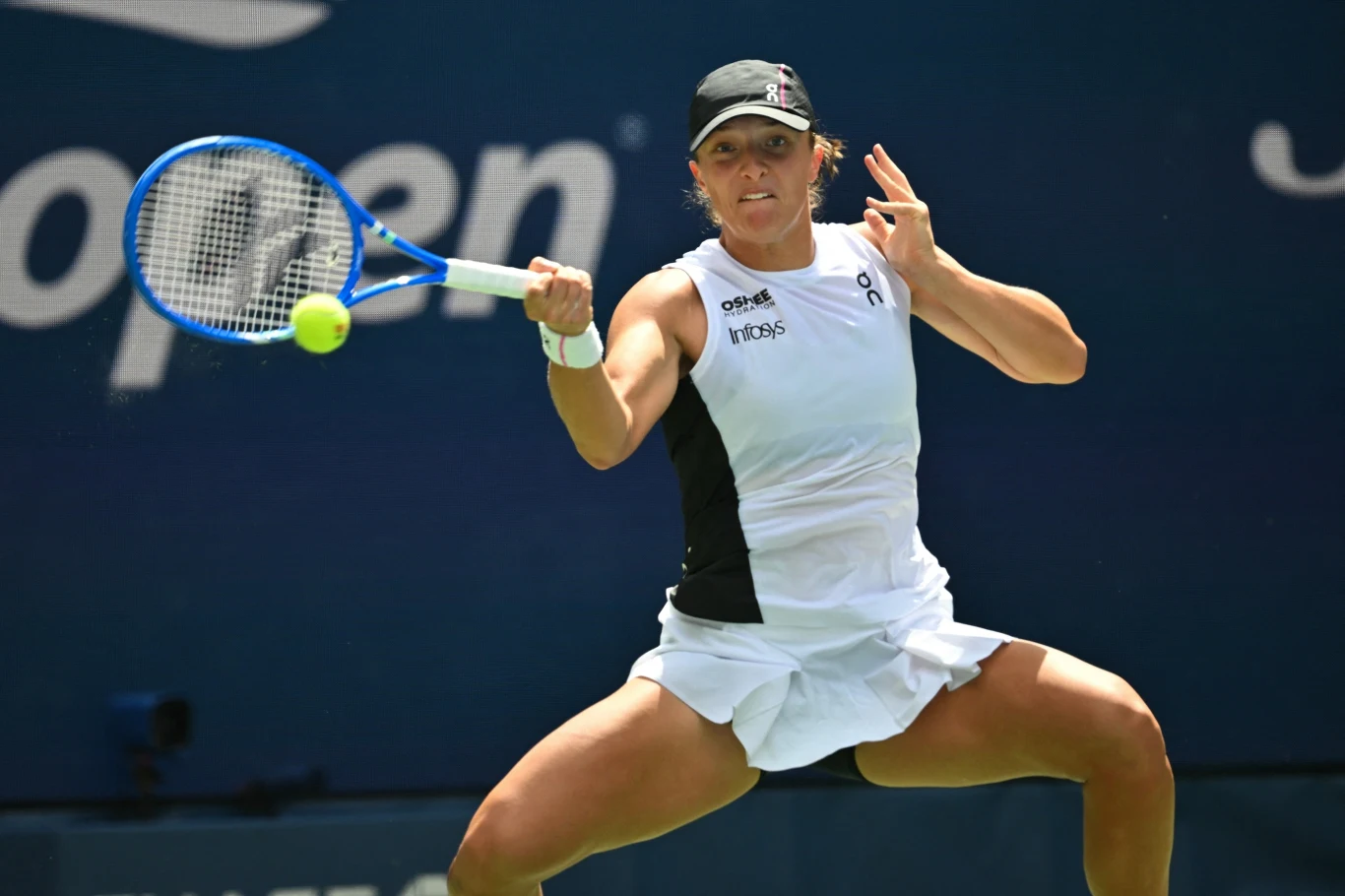 Zawodniczka tenisowa w białej sukience sportowej odbija piłkę rakietą podczas dynamicznej akcji na korcie US Open, widoczny jest intensywny wyraz skupienia i profesjonalizmu.