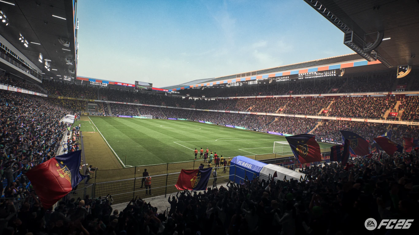 EA Sports FC 26 Tłum kibiców na trybunach dużego stadionu piłkarskiego, powiewające flagi drużynowe, na murawie piłkarze przygotowują się do meczu, jasne niebo i imponująca infrastruktura stadionowa.