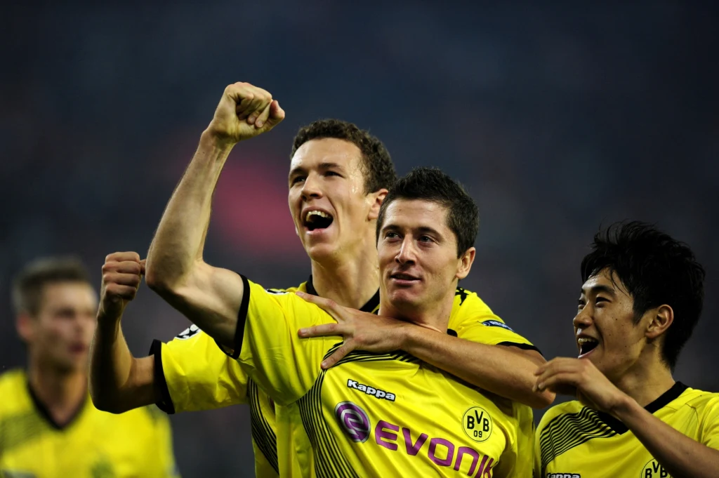 Robert Lewandowski zamiast do Genoi trafił do Borussii Dortmund Trzech piłkarzy w żółto-czarnych koszulkach Borussia Dortmund świętuje zwycięstwo, wyrażając radość gestami i mimiką twarzy, otoczonych stadionowym oświetleniem.