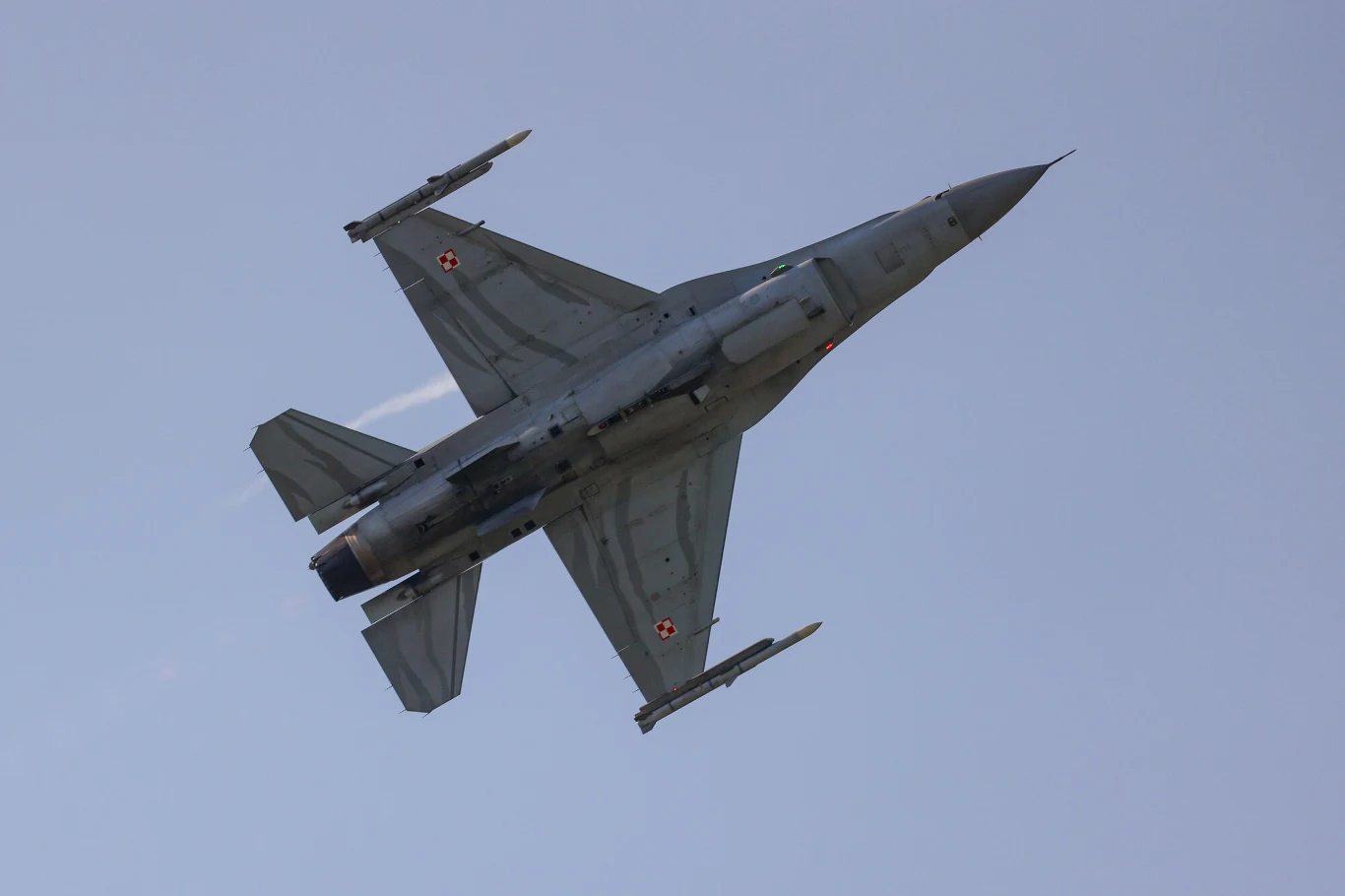 Zmasowany atak Rosji na Ukrainę. Polska poderwała myśliwce, zdj. ilustracyjne Myśliwiec wojskowy typu F-16 z polskimi oznaczeniami lotniczymi lecący na tle czystego nieba, widoczny z dołu pod kątem, wyraźnie zaznaczone uzbrojenie na skrzydłach.