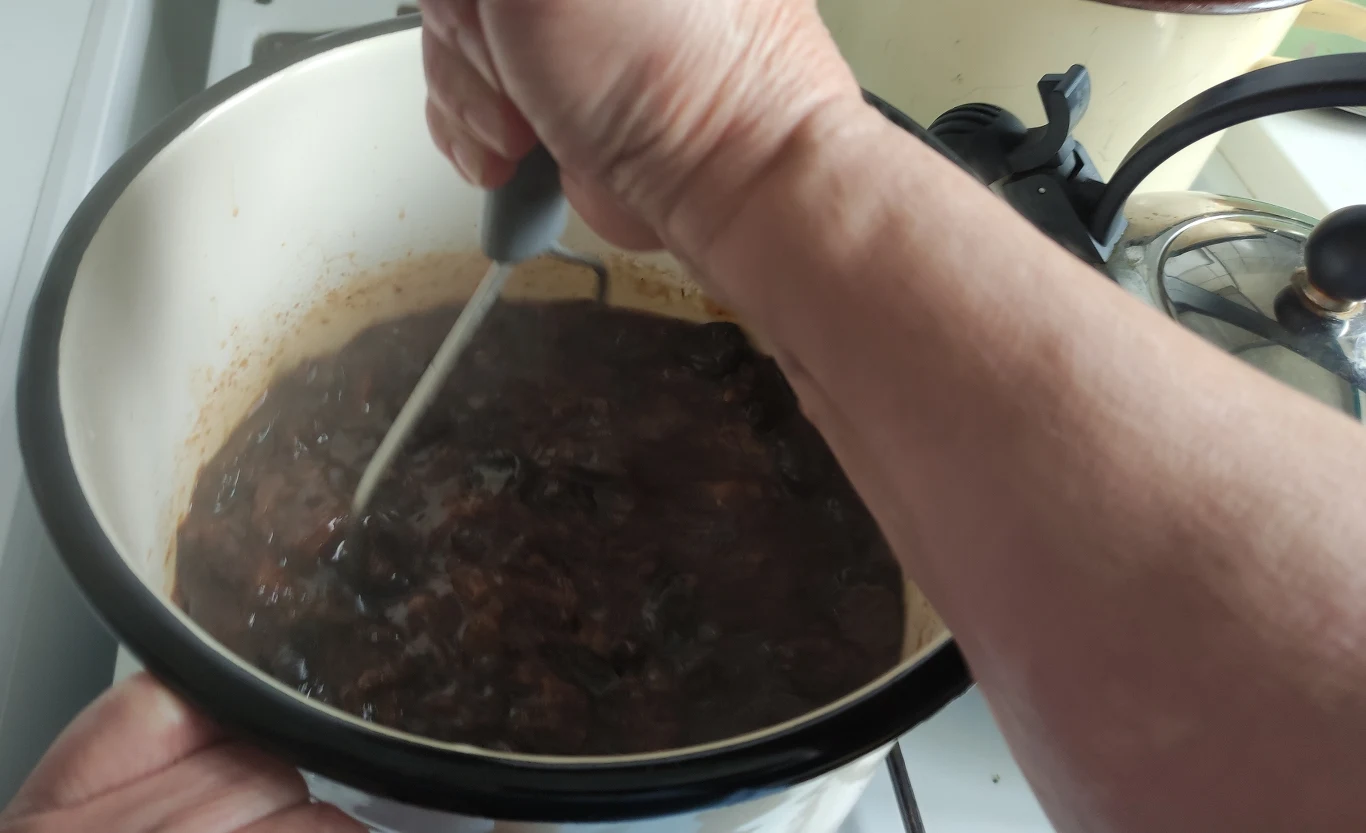 Gotowanie potrawy w dużym emaliowanym garnku na kuchence, ręka osoby energicznie miesza zawartość ciemnej potrawy łyżką.