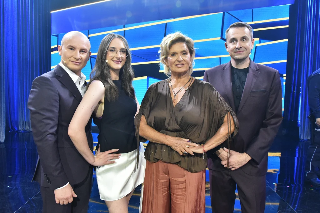 Ewa Kasprzyk i Kabaret K2 Cztery osoby stojące obok siebie na scenie, ubrani elegancko, na tle niebiesko-żółtej scenografii z geometrycznymi podświetleniami.