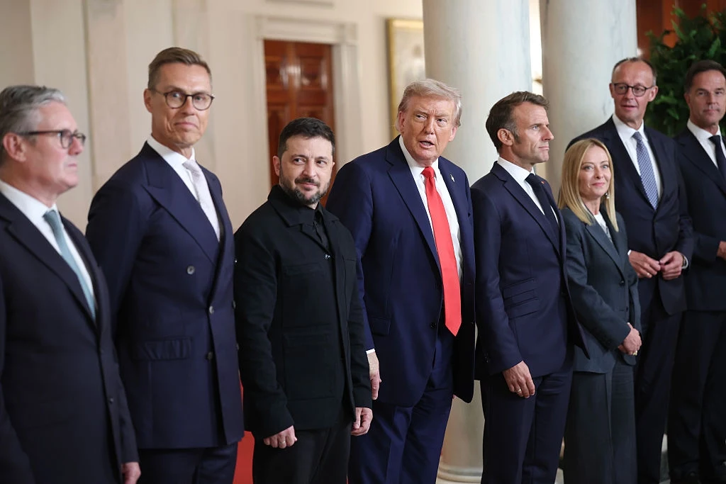 Spotkanie przywódców europejskich, Ukrainy i USA w Białym Domu Grupa siedmiu polityków w eleganckich garniturach i formalnych ubraniach stoi obok siebie w jasnym wnętrzu, część osób patrzy w stronę obiektywu, atmosfera oficjalnego spotkania.