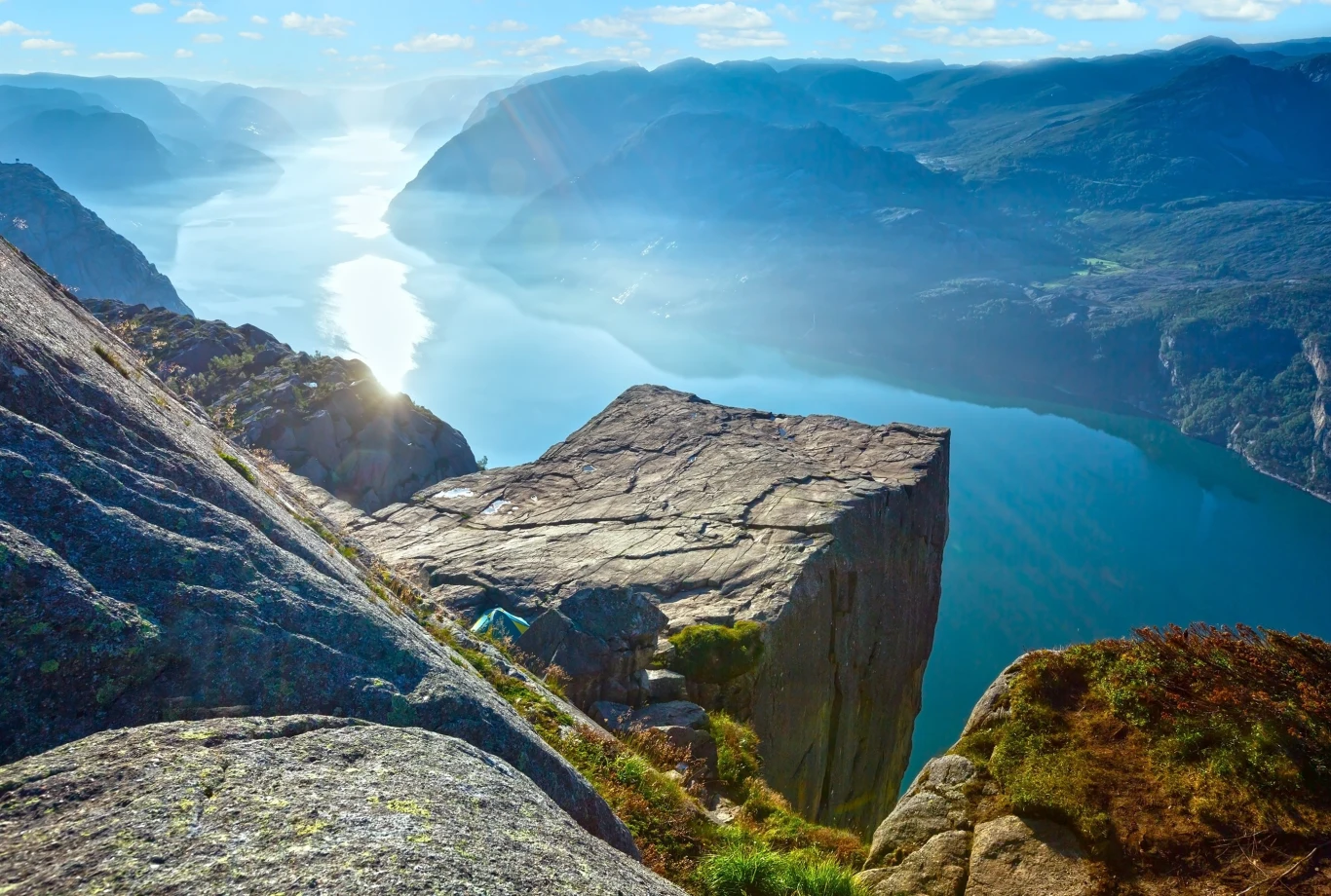 Słynna półka skalna Preikestolen nad błękitnym fiordem, otoczona stromymi klifami, z rozległym widokiem na wodę i góry w tle skąpane w promieniach słońca.