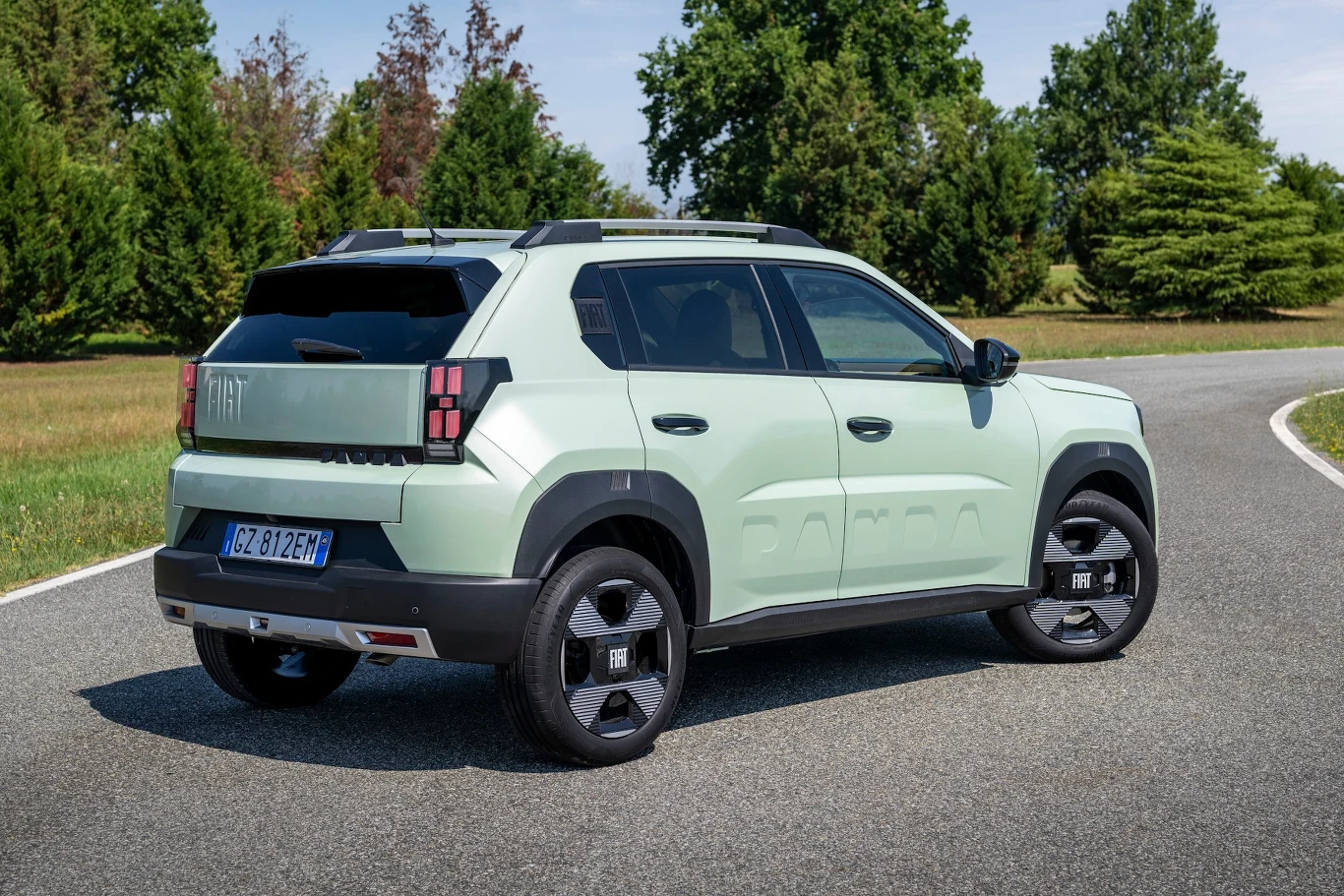 Fiat Grande Panda Jasnozielony samochód typu SUV marki Fiat stoi na zakręcie asfaltowej drogi, otoczony zielonymi drzewami i krzewami w naturalnym, letnim krajobrazie.