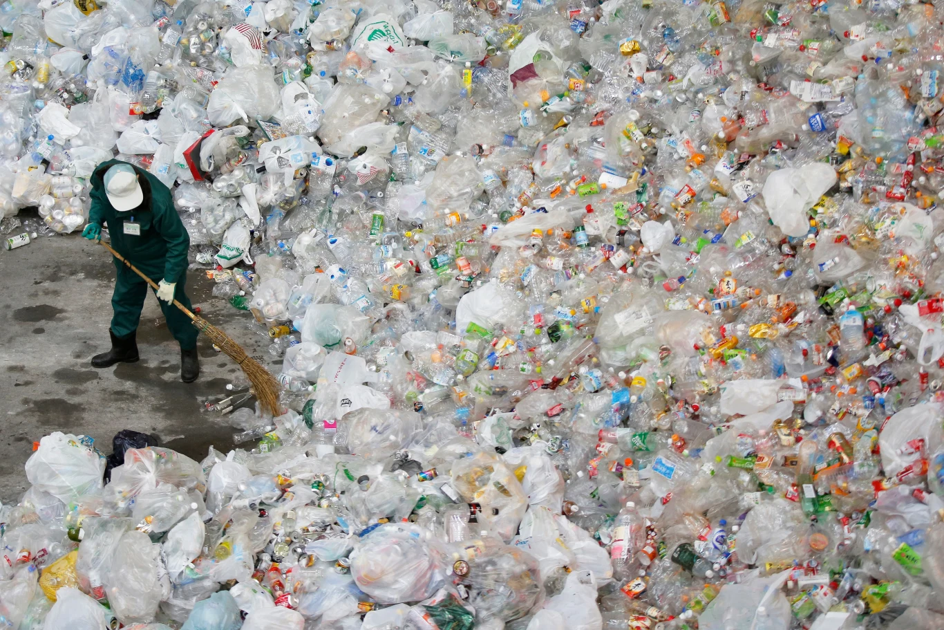Amerykańscy naukowcy opracowali nową metodę recyklingu najgorszego plastiku Pracownik w zielonym kombinezonie i białym kasku zamiata ogromną ilość plastikowych butelek i worków, które tworzą rozległą hałdę śmieci.
