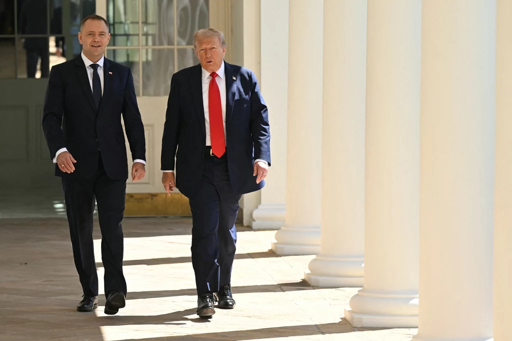 Prezydenci Polski i Stanów Zjednoczonych: Karol Nawrocki i Donald Trump Dwóch mężczyzn w garniturach idzie razem wzdłuż kolumnady, oświetleni światłem dziennym, tło stanowią jasne kolumny oraz szklane drzwi.