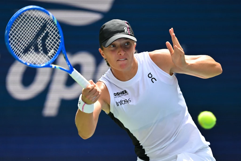 Iga Świątek rywalizowała z Amandą Anisimovą o półfinał US Open 2025 Zawodniczka tenisowa w białym stroju z niebieską rakietą tenisową w trakcie gry, skupiona na piłce lecącej z prawej strony ujęcia, na tle niebieskiego kortu