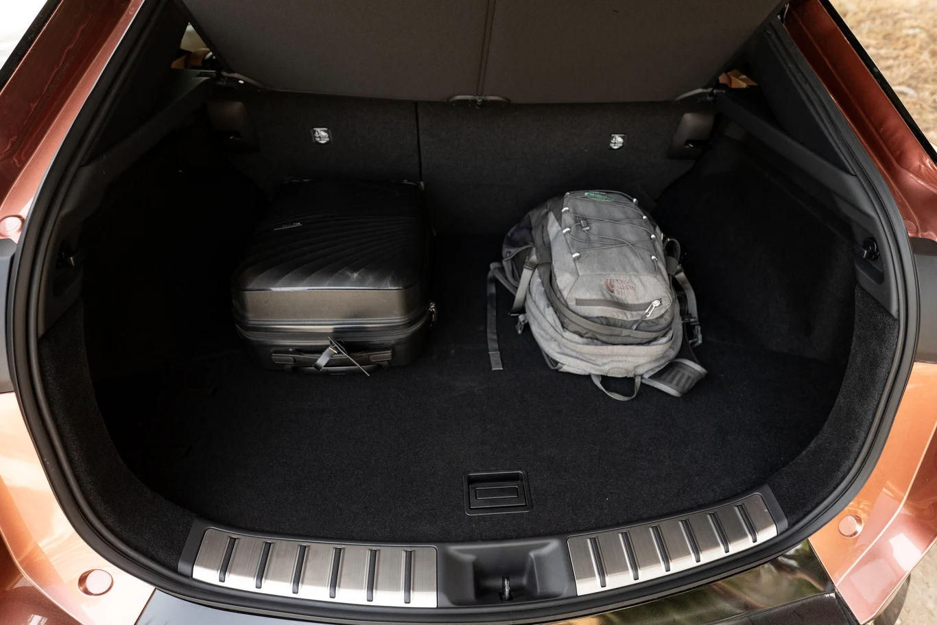 Otwarty bagażnik samochodu z walizką w czarnym kolorze oraz szarym plecakiem ustawionymi na wykładzinie bagażnika.