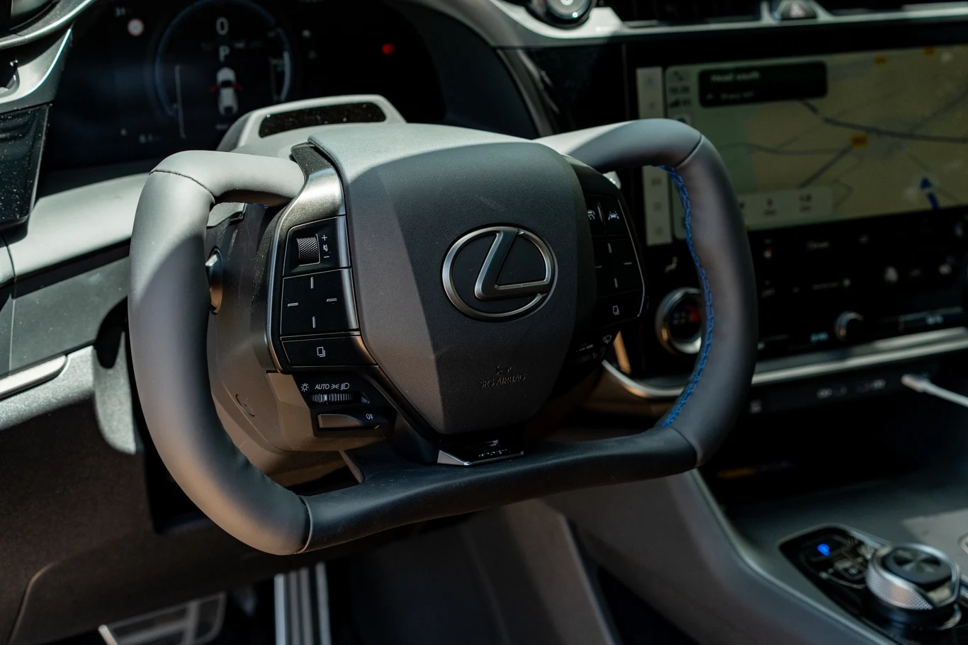 Nowoczesna kierownica z logo marki Lexus oraz fragment konsoli centralnej z wyświetlaczem nawigacji i elementami sterowania samochodu