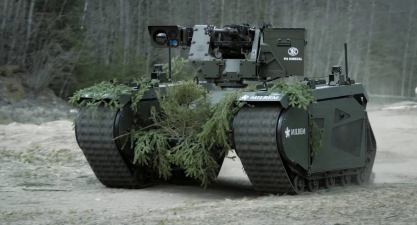 Europa wysyła Ukrainie rekordową flotę THeMIS-ów. Czy estońskie roboty zmienią pole walki? Bezzałogowy pojazd gąsienicowy pokryty gałęziami dla kamuflażu, wyposażony w sprzęt militarny, porusza się po leśnej drodze, w tle widoczny jest las.