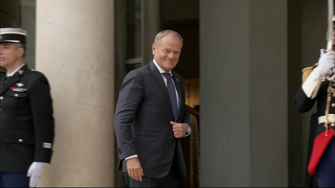 Koalicja chętnych w Paryżu. Tematem bezpieczeństwo Ukrainy Elegancko ubrany mężczyzna w garniturze wychodzi z budynku, po jego bokach stoją umundurowani funkcjonariusze w oficjalnych strojach typu ceremonialnego.