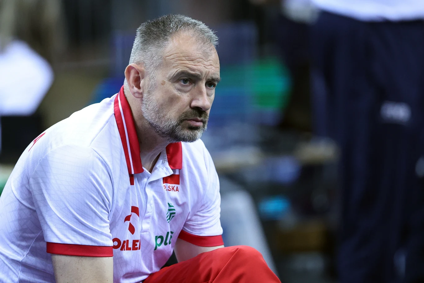 Trener Nikola Grbić podczas memoriału Huberta Jerzego Wagnera w Krakowie Mężczyzna w średnim wieku w koszulce z napisem 'Polska', siedzi w skupieniu, patrząc przed siebie; otoczenie wskazuje na halę sportową lub wydarzenie sportowe.