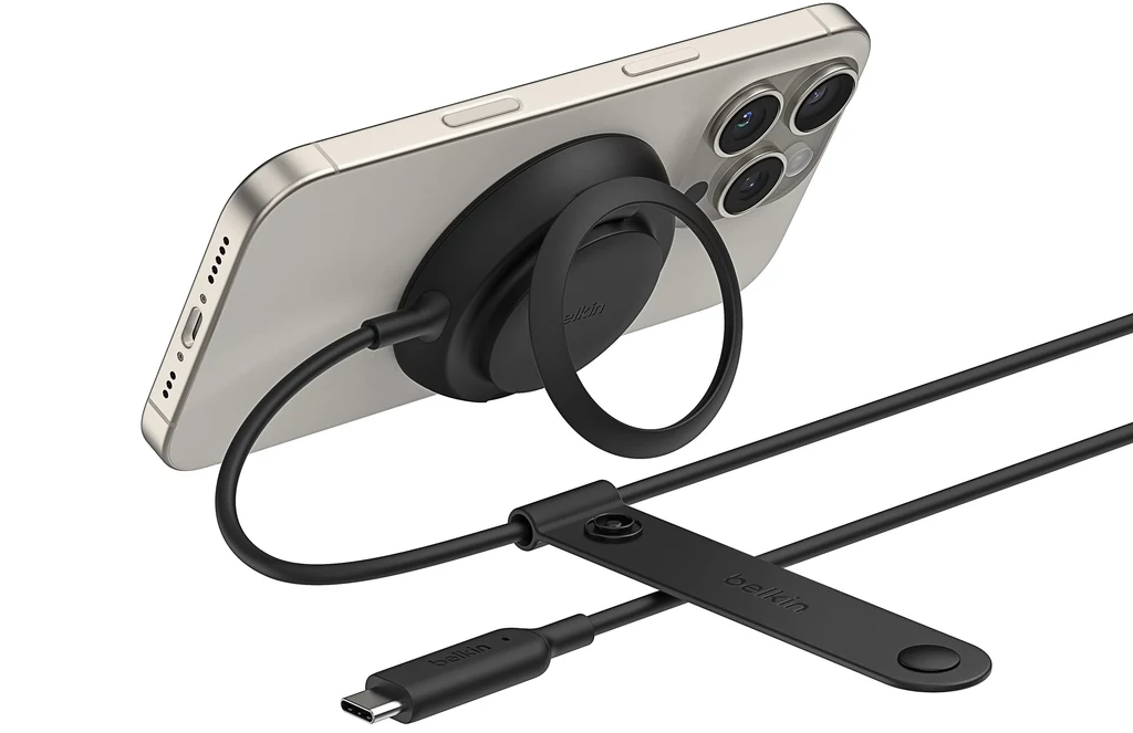 Belkin UltraCharge Magnetic Charger to ładowarka bezprzewodowa zgodna ze standardem Qi2 25W. Białe nowoczesne smartfon z trzema obiektywami kamery na tylnej części jest ładowany za pomocą czarnej magnetycznej ładowarki bezprzewodowej podłączonej do kabla USB-C; obok widoczny jest uchwyt do organizacji kabla z logo belkin.