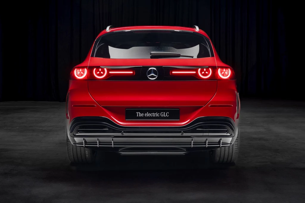 W tylnych lampach również zaszyto logo Mercedesa Czerwony samochód typu SUV marki Mercedes-Benz, widok od tyłu, z wyrazistymi światłami LED i tablicą informacyjną z napisem 'The electric GLC', ustawiony na ciemnym tle.