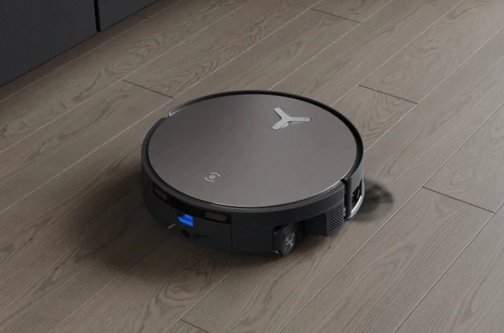 Ecovacs Deebot X11 Omnicyclone to robot sprzątający z obsługą szybkiego ładowania GaN. Robot sprzątający o okrągłym kształcie poruszający się po jasnej, drewnianej podłodze, wyposażony w czujniki i nowoczesny design.