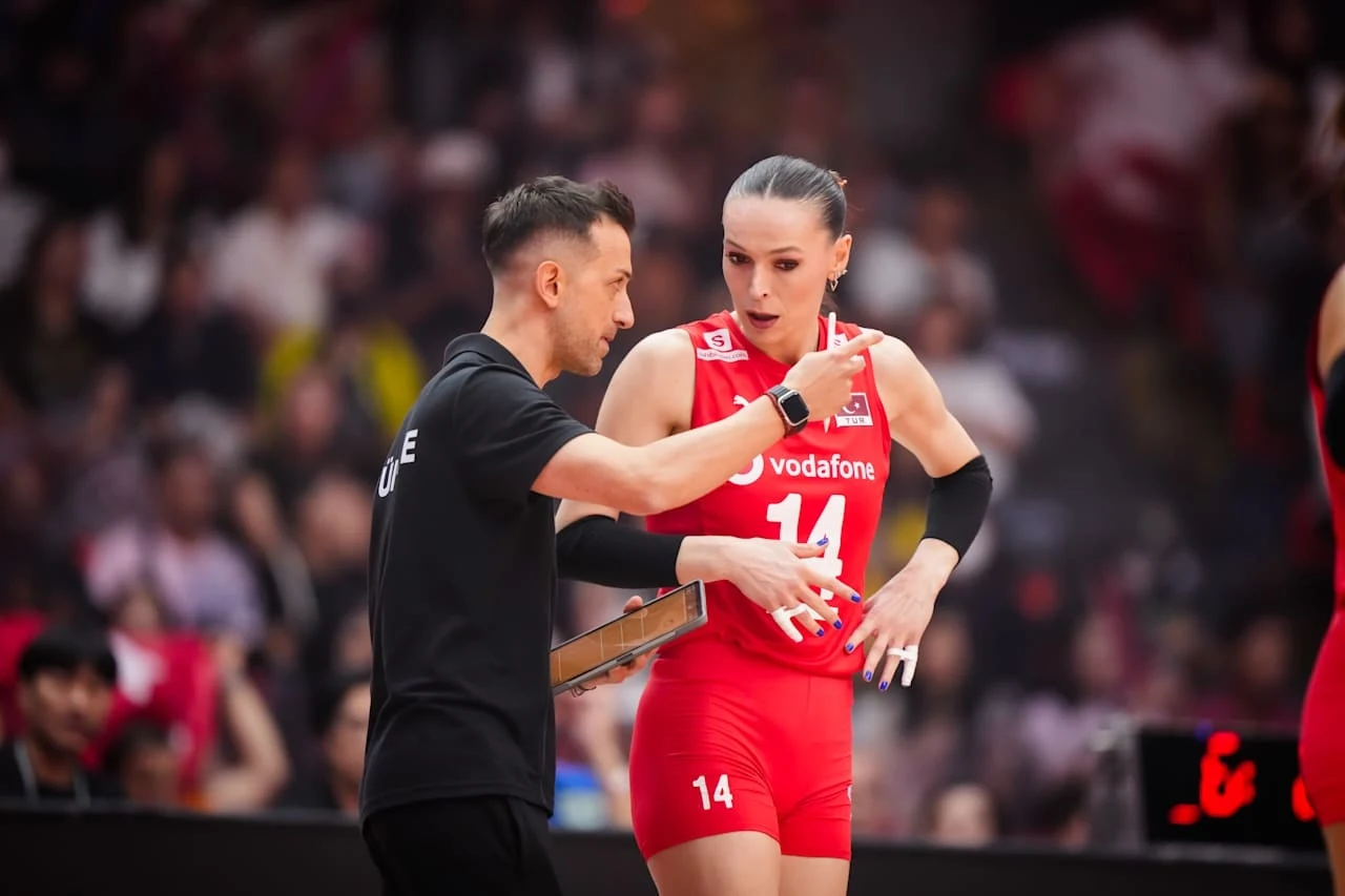 Trener Daniele Santarelli i kapitan Turczynek Eda Erdem Trener udziela wskazówek siatkarce ubranej w czerwony strój z numerem 14 podczas meczu siatkówki, wokół widoczni są kibice na trybunach.
