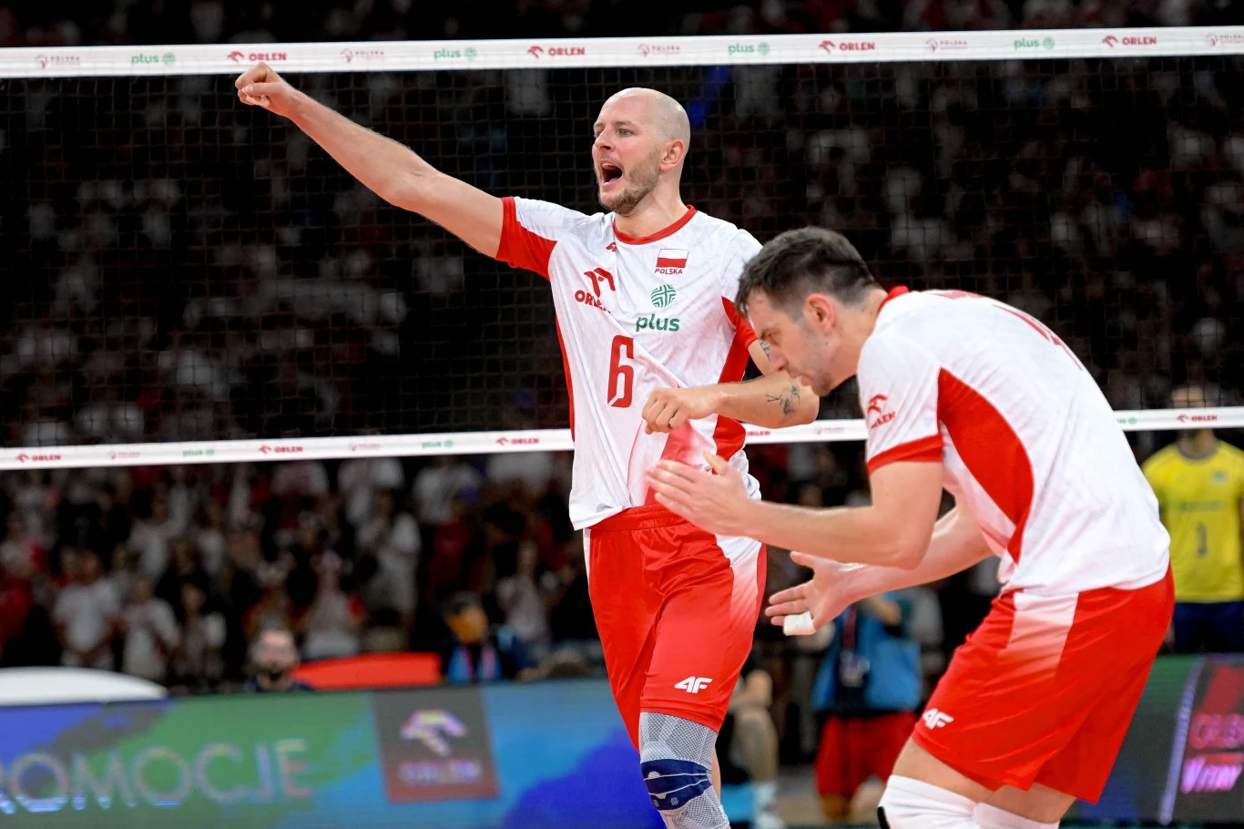 Bartosz Kurek rozgrywał się z każdym setem, podobnie jak cały polski zespół. Apogeum nastąpiło w 2. partii, w której nasz zespół rozbił Brazylię 25:14 Dwóch siatkarzy w biało-czerwonych strojach drużyny narodowej świętuje zdobyty punkt na boisku, wokół widoczna publiczność i siatka, atmosfera sportowej rywalizacji i radości.