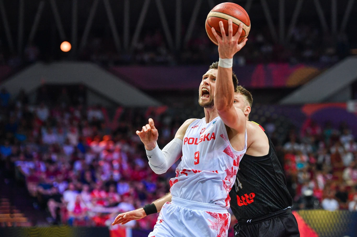 Mateusz Ponitka w walce z Belgami Zawodnik reprezentacji Polski w koszykówce podczas dynamicznej akcji pod koszem, z piłką w jednej ręce próbuje zdobyć punkty w starciu z obrońcą drużyny przeciwnej.