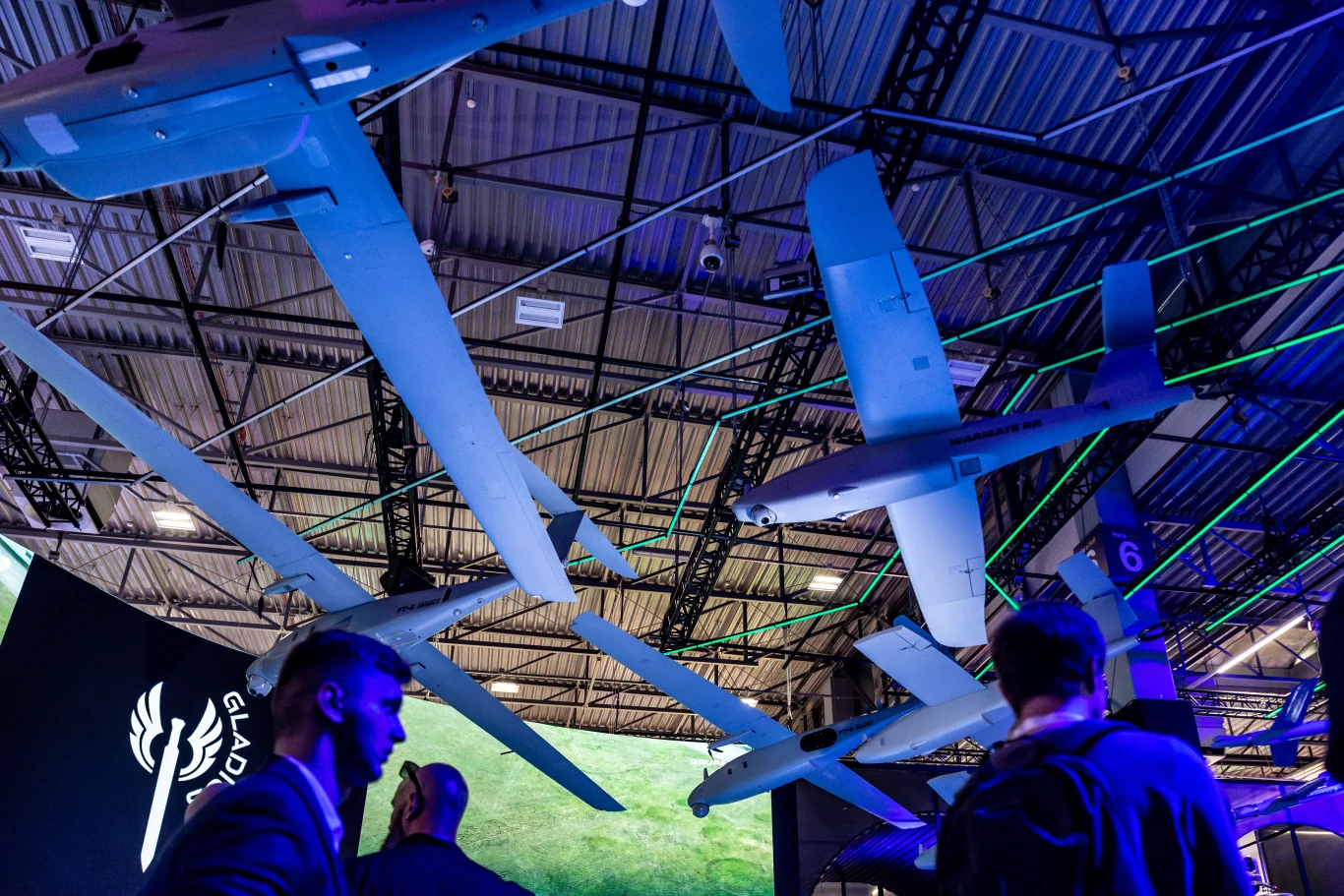 Podczas Międzynarodowego Salonu Przemysłu Obronnego 2025 w Kielcach zwiedzający mogli zobaczyć wiele innowacyjnych technologii wojskowych (zdj. poglądowe) Kilka bezzałogowych dronów zawieszonych pod dachem hali wystawienniczej, oświetlone kolorowymi światłami, w tle znajdują się osoby obserwujące prezentację nowoczesnych technologii.