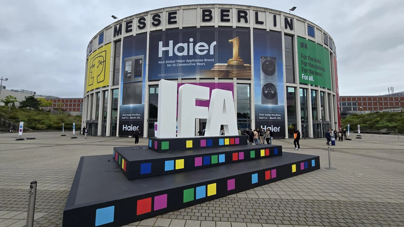 IFA 2025 w Berlinie. Sztuczna inteligencja w domu. Nowoczesny budynek Messe Berlin z dużym napisem IFA na podwyższeniu, otoczony kolorowymi blokami, na tle banerów reklamujących markę Haier i wydarzenie technologiczne, wokół spacerują pojedyncze osoby.