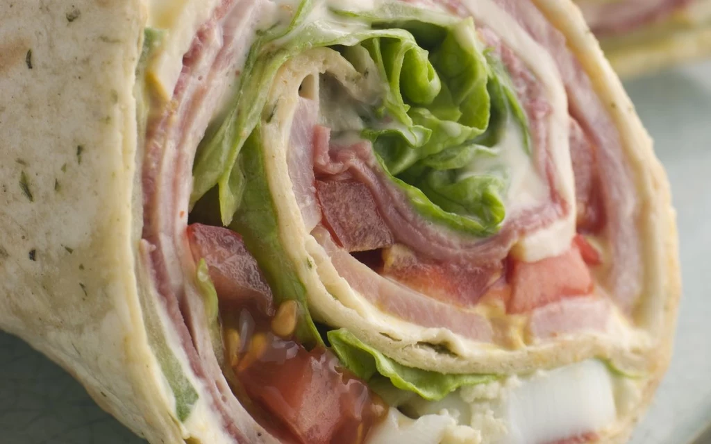 Wrapy są proste i szybkie w przygotowniu Pyszny wrap z tortilli nadziany warstwami świeżej sałaty, soczystych pomidorów, plasterków mięsa i kremowego sosu.
