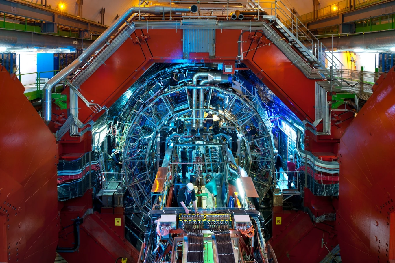 ALICE w CERN. To dla niego polski student projektuje nowy detektor FoCal-H Ogromna struktura naukowa o symetrycznej budowie, pełna instalacji, przewodów i złożonych elementów metalowych oświetlonych niebieskimi i czerwonymi światłami, w centrum widoczni pracownicy pracujący wewnątrz urządzenia.